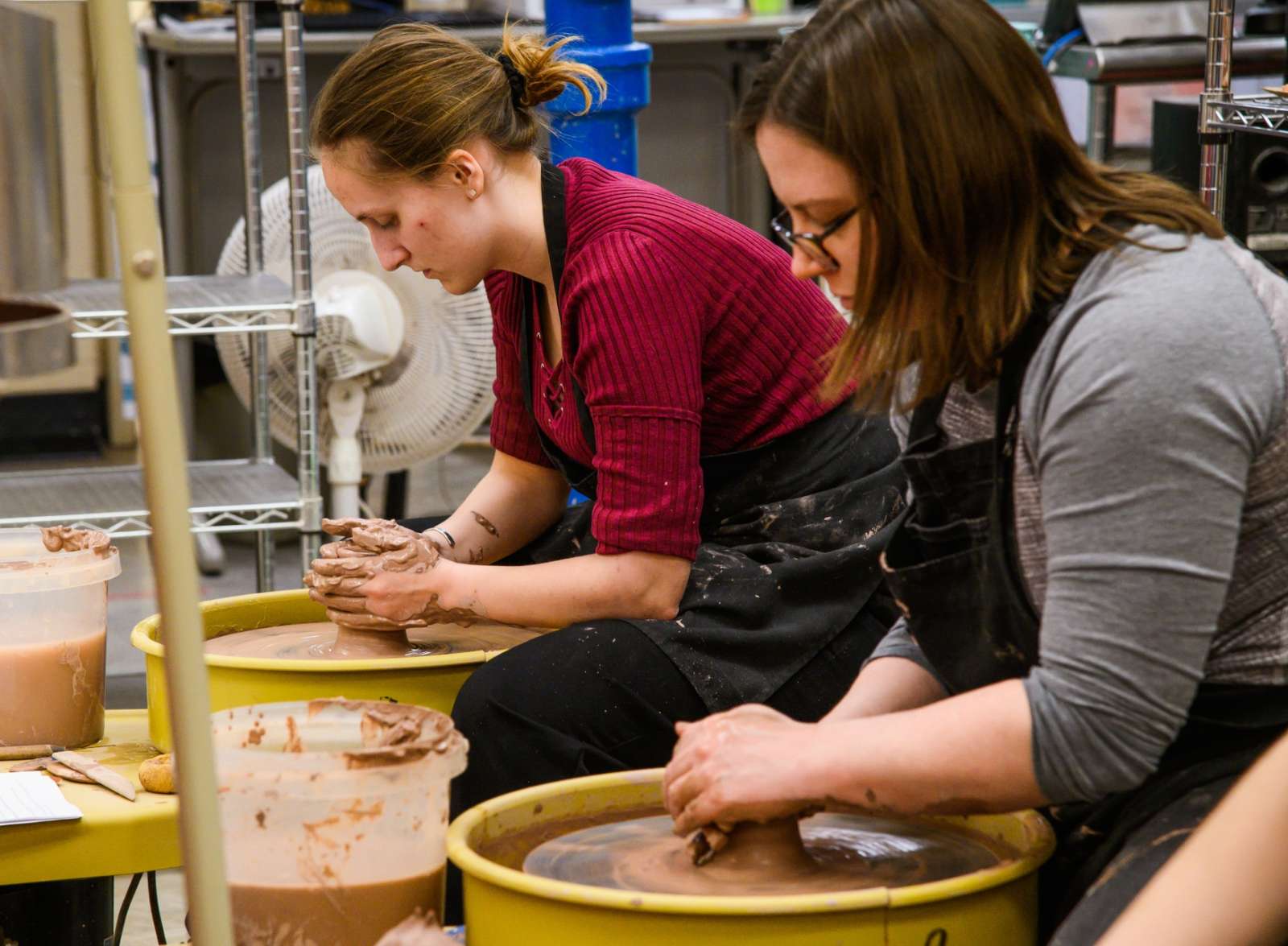 two students working at the pottery wheels in the workspace